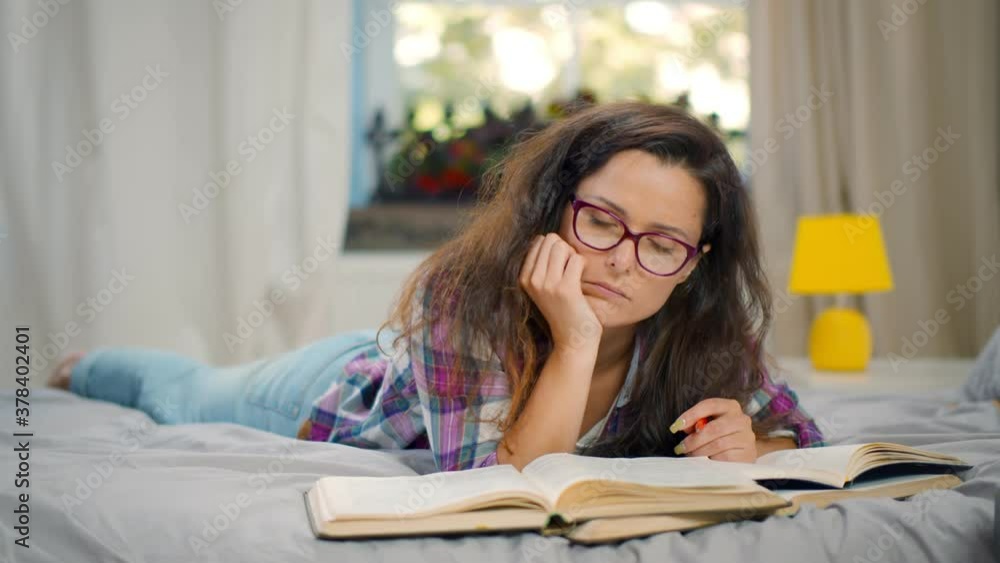 Tired female student falling asleep doing homework on bed Tired female student falling asleep doing homework on bed