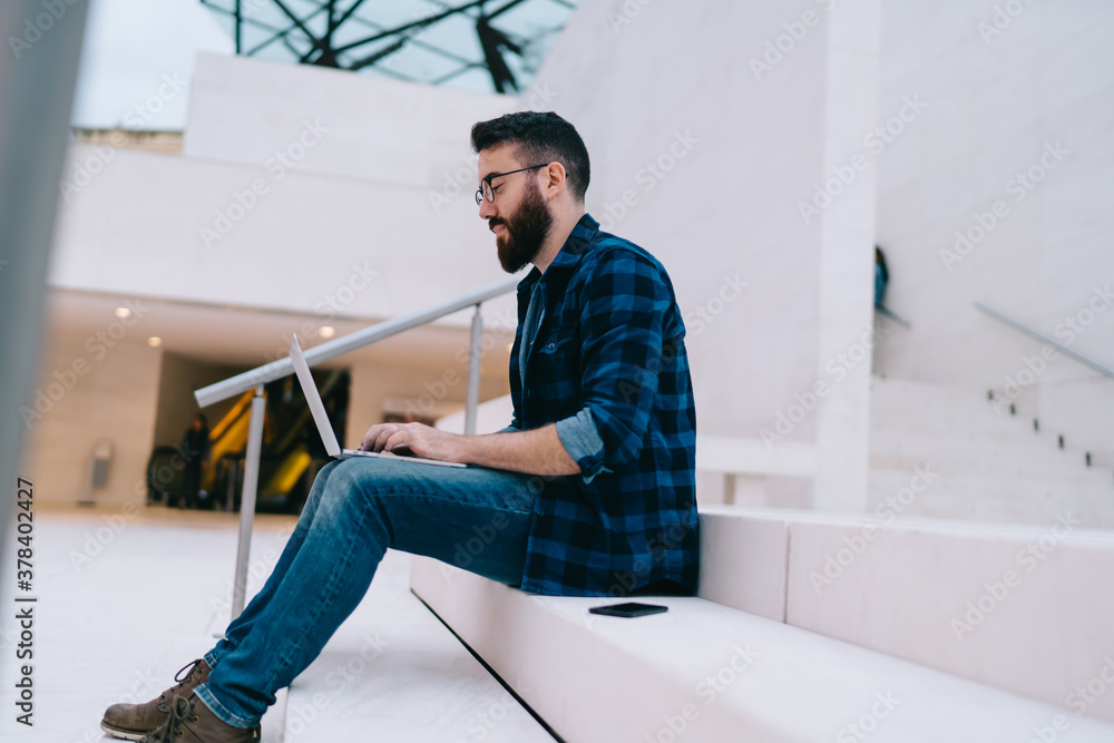 Concentrated man with laptop sitting on stairs inside modern building
