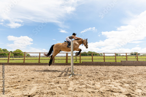 Young woman riding a horse and jumping over the hurdle