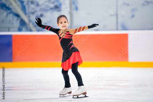Foto little girl figure skater in light pink tracksuit with smile skates on the ice on an indoor skating rink