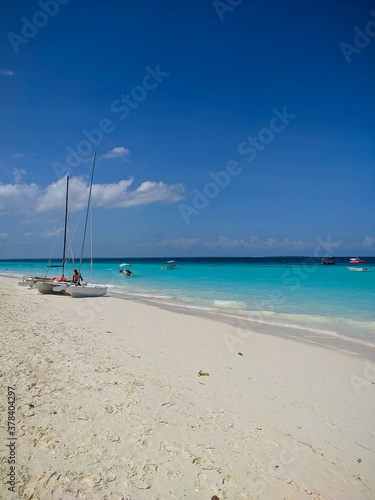 Zanzibar  Tanzania - December 3  2019  Nungwi beach in Zanzibar  bright blue sea and blue sky on a beautiful white beach. The sailors  boats are on the shore for fishing and recreation.  Vertical