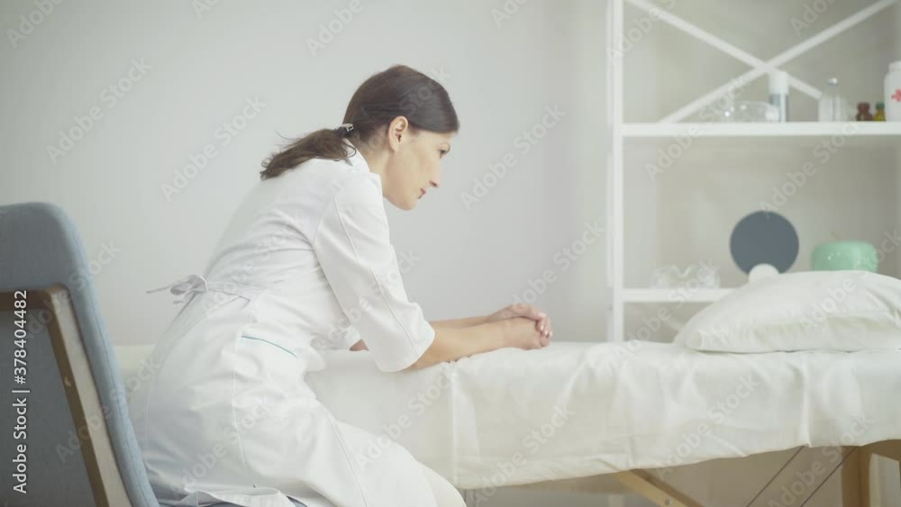 Side view of exhausted Caucasian woman sitting in hospital ward leaning head on hand. Portrait of tired female doctor at workplace. Desperate physician on Covid-19 pandemic. Side view of exhausted Caucasian woman sitting in hospital ward leaning head on hand. Portrait of tired female doctor at workplace. Desperate physician on Covid-19 pandemic.