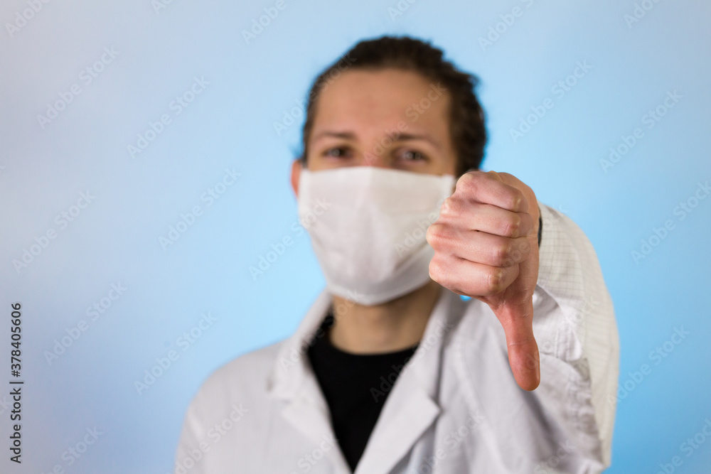 An adult male dressed in a white lab coat with a protective face mask on while giving a thumbs down. Ready to work in a clean room or laboratory