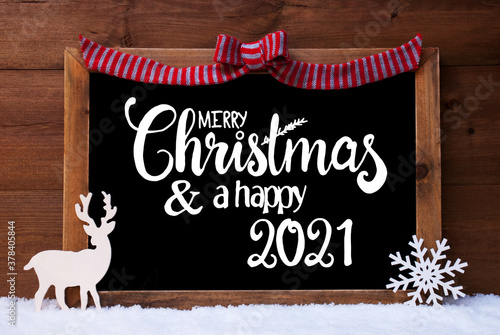 Chalkboard With English Calligraphy Merry Christmas And A Happy 2021. Christmas Decoration Like Deer And Bow. Wooden Background With Snow photo