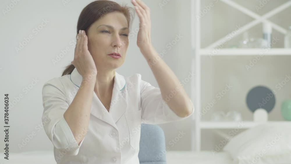 Portrait of stressed doctor with headache holding temples with hands and sighing. Tired Caucasian woman having symptoms of Covid-19 infectious disease after work with ill patients. Portrait of stressed doctor with headache holding temples with hands and sighing. Tired Caucasian woman having symptoms of Covid-19 infectious disease after work with ill patients.