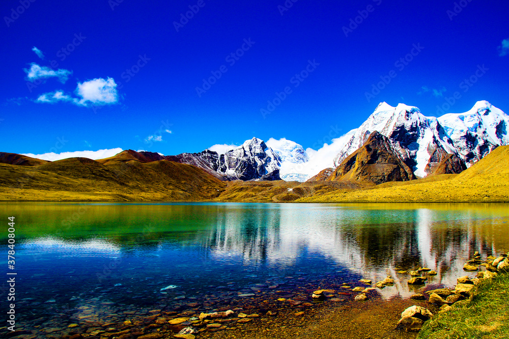 pebbles on a ake shore with blue skies reflecting on still blue waters. scenic himalayan landscape