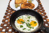 Fried eggs in a rustic iron pan, toast on a dish for breakfast