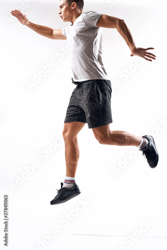 athlete man in sneakers shorts and a t-shirt on a light background and running to the side in full growth