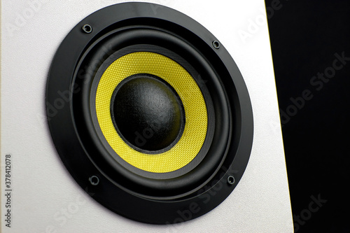 White audio speaker on a black background. Subwoofer, close-up. Minimalistic audio speaker with a yellow subwoofer.