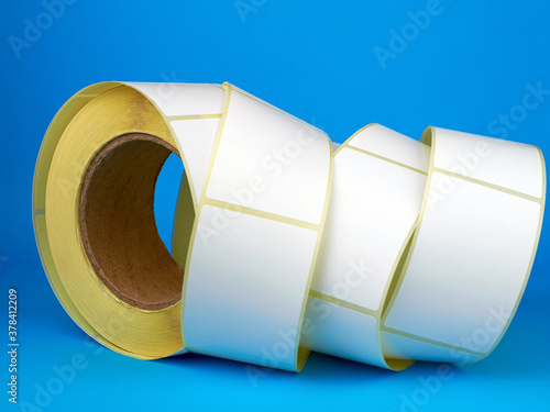 White roll of labels for thermal perforation on a blue background. Babina of self-adhesive stickers. Self-adhesive white label roller for printing or manufacturing. photo