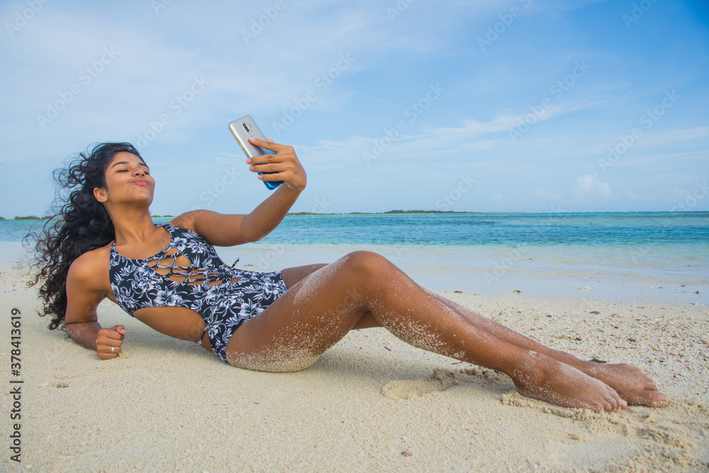 Hispanic teenager girl with phone smiling enjoy summer time at luxury beach