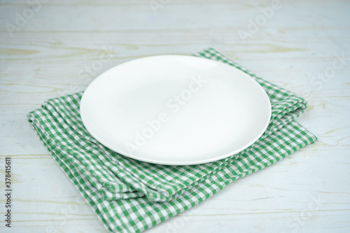 White empty ceramic plate on a green kitchen plaid towel.