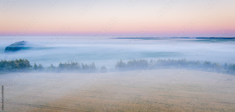 Morning fog in the meadows during sunrise in the countryside, aerial view height of the landscape on the horizon, a trees in the fog.