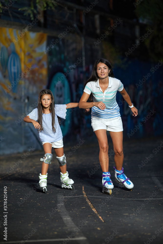 young mother and her little daughter rollerskating in the evening. family have fun