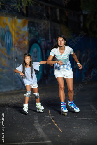 young mother and her little daughter rollerskating in the evening. family have fun