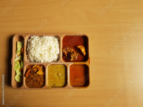 indian chicken thali with rice dal chicken salad vegetable curry on a plastic segmented plate in wooden background photo