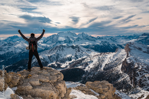 Triumphant man conquer the summit standing in front of beautiful landscape with raised hands, Cortina Italy holiday destination. Scenic mountain panorama, iconic winter holiday/vacation desinations