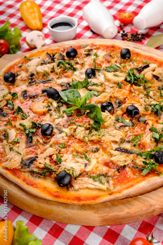 Rustic pizza with chicken meat, cheese, tomato, olive, mushrooms and tomatoes sauce, served on a wooden board for a dinner in italian restaurant background, top view. 