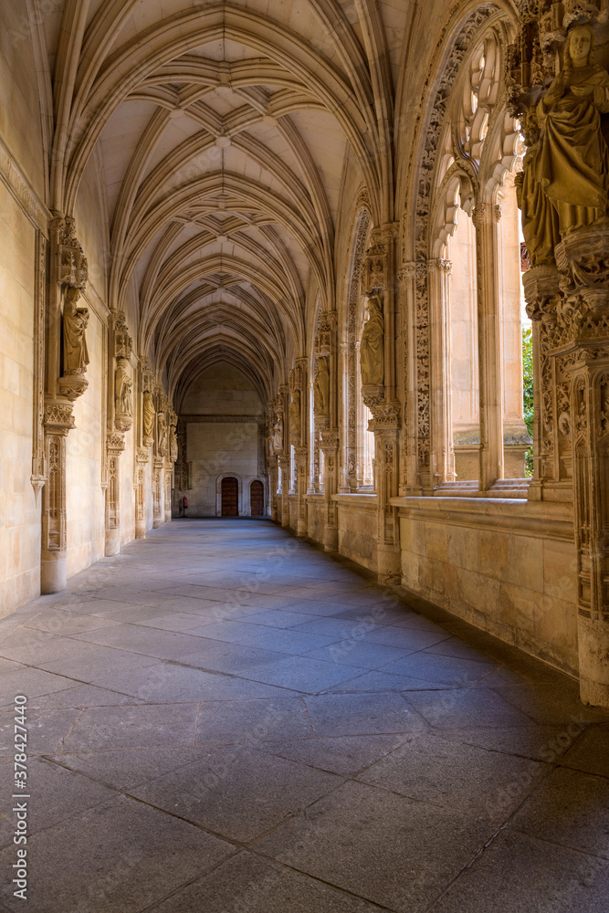Gothic Cloister - A wide-angle vertical view of evening sunlight shining in lower cloister of the 15th-century Isabelline Gothic style church Monastery of Saint John of the Monarchs, Toledo, Spain.