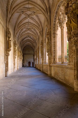 Gothic Cloister - A wide-angle vertical view of evening sunlight shining in lower cloister of the 15th-century Isabelline Gothic style church Monastery of Saint John of the Monarchs, Toledo, Spain.