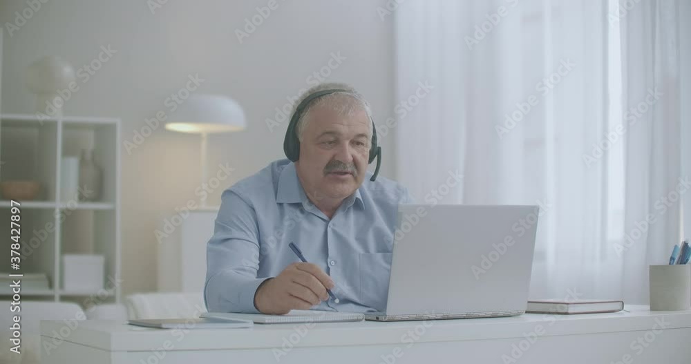 middle-aged man is communicating by online chat with colleagues and employees from home using laptop and headphones middle-aged man is communicating by online chat with colleagues and employees from home using laptop and headphones