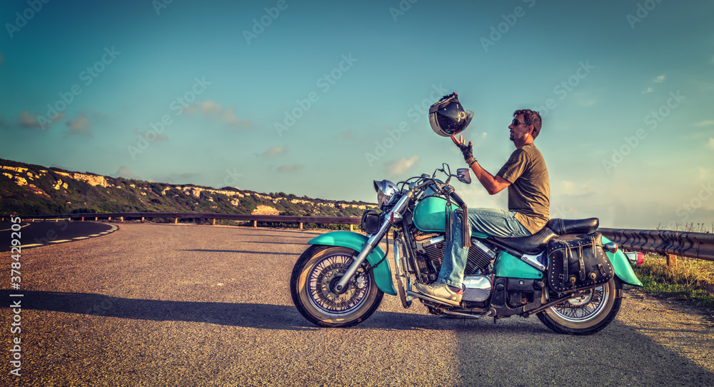 Fototapeta premium Biker on a classic turquoise motorcycle playing with the helmet
