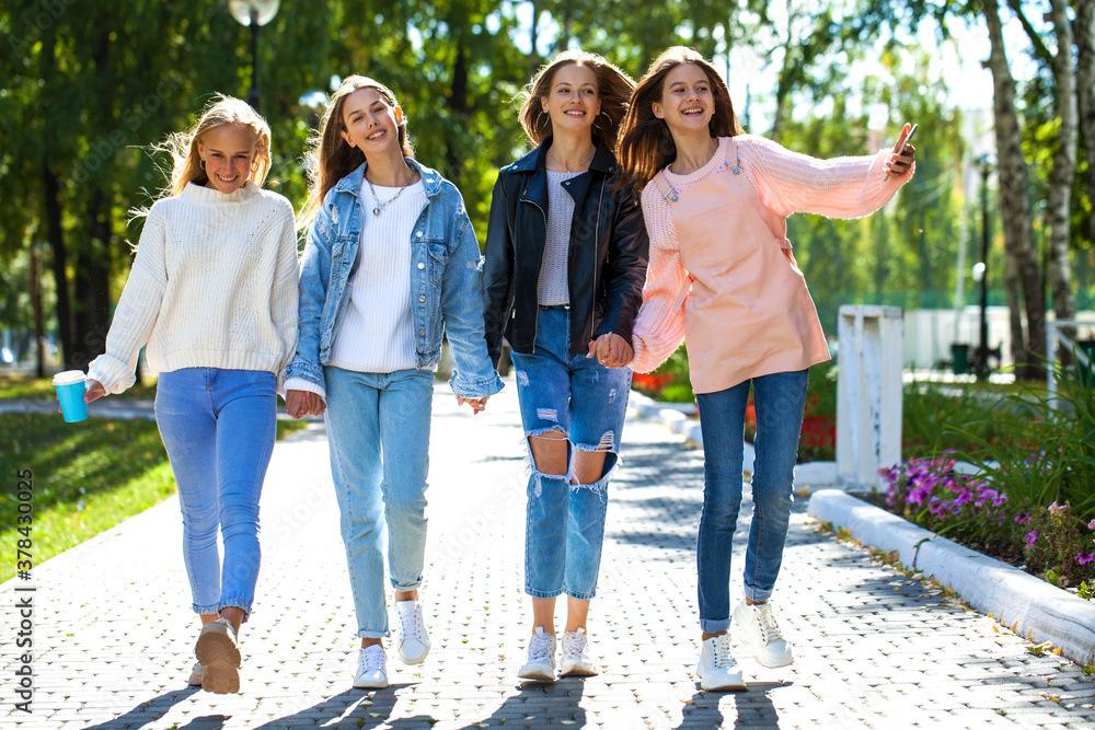 Four happy young girlfriends walking in autumn park