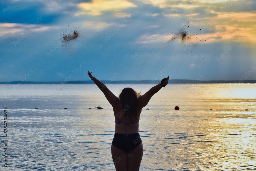 Rear view of a woman throwing sand in the air on the beach at sunset