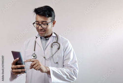 male indian doctor in white coat and stethoscope touching smart phone