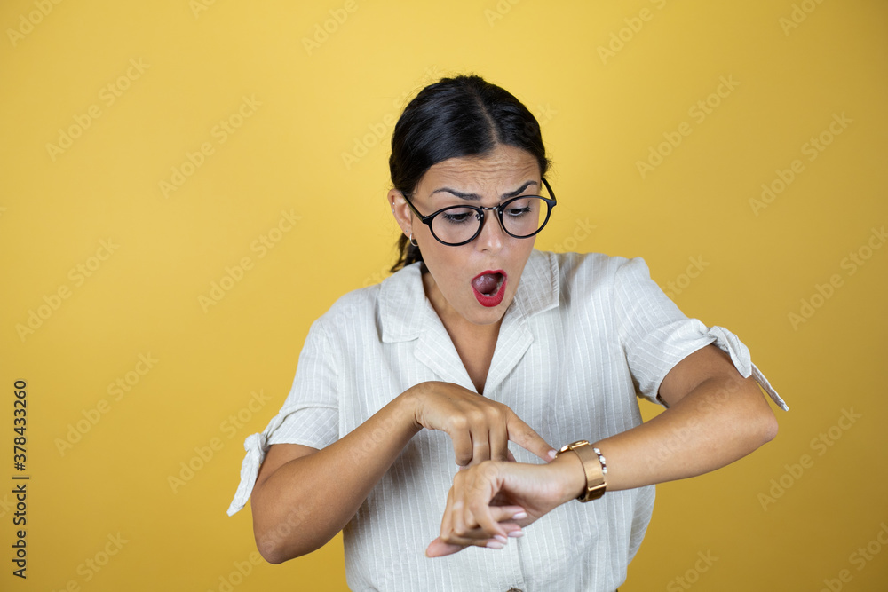Beautiful woman over yellow background surprised and pointing the watch because it's late