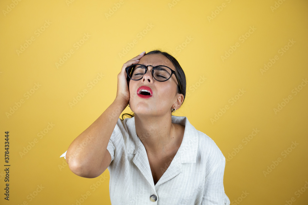 Beautiful woman over yellow background putting one hand on her head smiling like she had forgotten something. Beautiful woman over yellow background putting one hand on her head smiling like she had forgotten something.