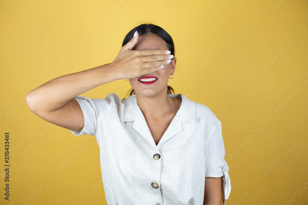 Beautiful woman over yellow background serious and covering her eyes with her hand. Beautiful woman over yellow background serious and covering her eyes with her hand.