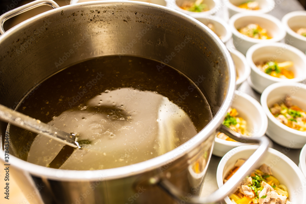 Pot of broth next to lined up bowl of chicken soup Pot of broth next to lined up bowl of chicken soup