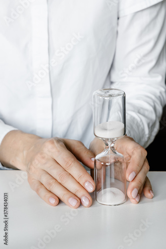 Hourglass in woman's hands, sand flowing through the bulb of sandglass measuring time. White minimal concept.