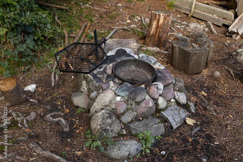 fireplace with empty brass pot and empty black grill between grey stones and brown forest floor, fireplaces offer hikers a cooking place to prepare their food, during the day, without people