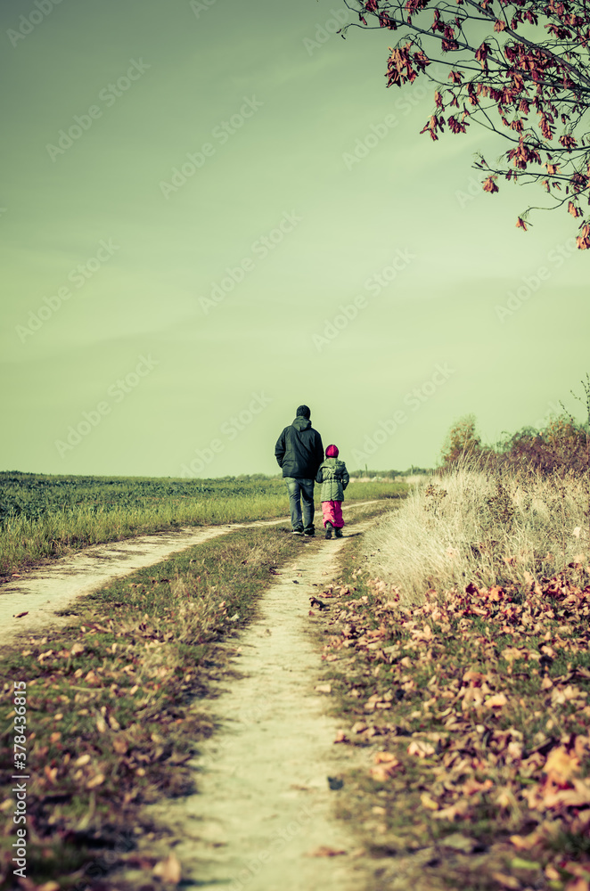 man and girl child walking together in autumnal colorful nature in rural path in sunny day with happy tranquil atmosphere
