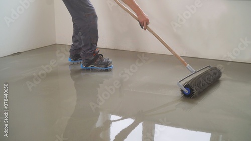 A worker rolls out the liquid floor with a trowel. Squeegee for distributing the mixture. The worker levels the liquid floor. Finishing works - Needle roller for bulk floor