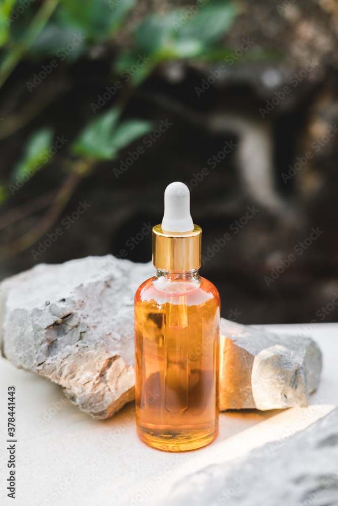Bottles of orange serum next to natural stones against a gray wall with grape leaves with natural light. Trendy style. Grape extract. Cosmetic mockup. Copyspace. Bottles of orange serum next to natural stones against a gray wall with grape leaves with natural light. Trendy style. Grape extract. Cosmetic mockup. Copyspace.
