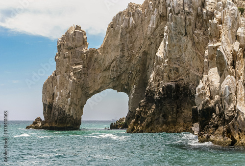 Cabo San Lucas, Mexico - April 22, 2008: South end of Baha California. Closeup of the Arch in beige rocks formation. Greenish ocean water in front under blue cloudscape.