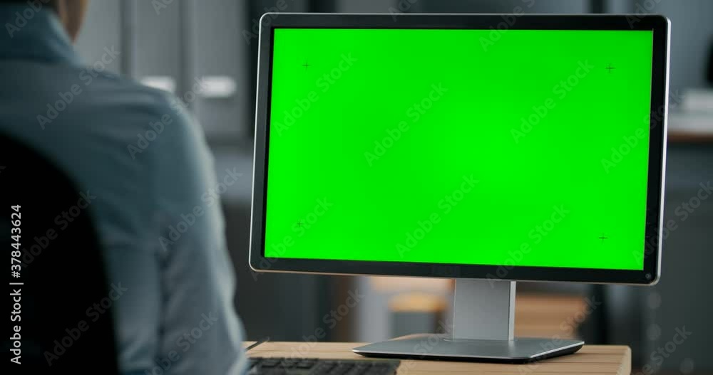 View from shoulder of mature lady in formal wear working on modern computer with blank green screen at office center. Concept of people and technology.