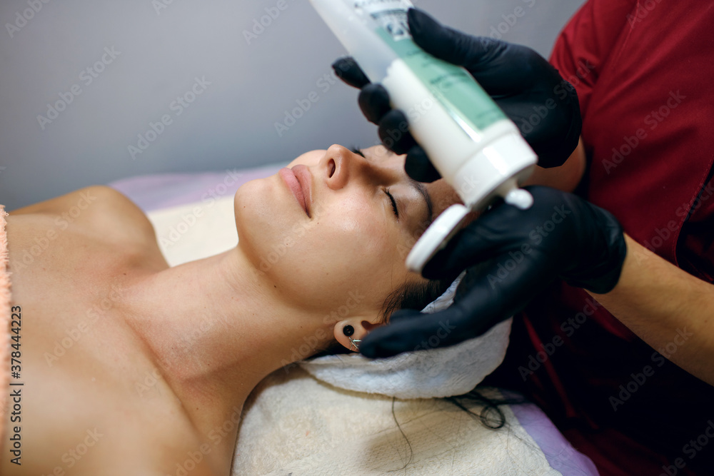Close-up of a brunette woman in a spa salon, a professional cosmitologist applies cream to the client's face. The concept of facial skin care and own body health Close-up of a brunette woman in a spa salon, a professional cosmitologist applies cream to the client's face. The concept of facial skin care and own body health