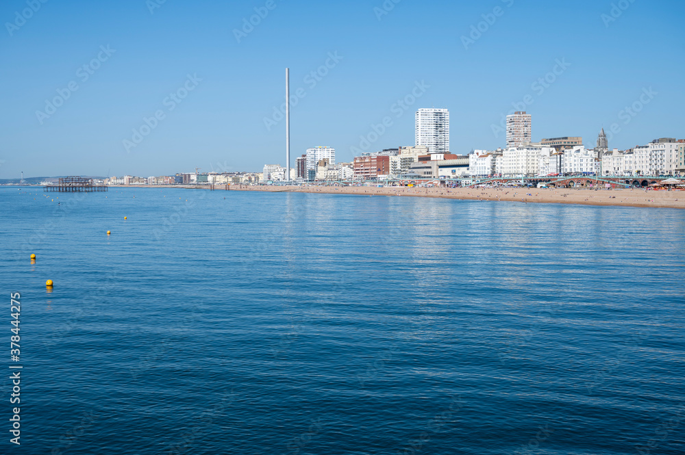 Brighton Seafront with elegant buildings and attraction in view on a warn and tranquil summer day with reflections in the calm water.