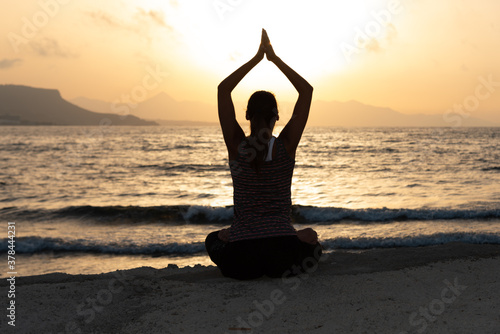 Silhouette, young woman with protective surgical face mask performs yoga stretching exercises at the beach at dusk during covid-19 coronavirus pandemic