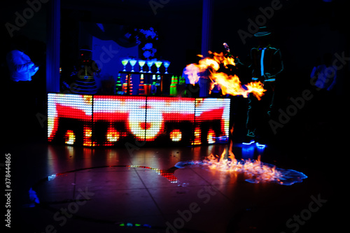 Professional barman and led light fire show. Silhouette of modern bartender shaking drink at night cocktail bar.