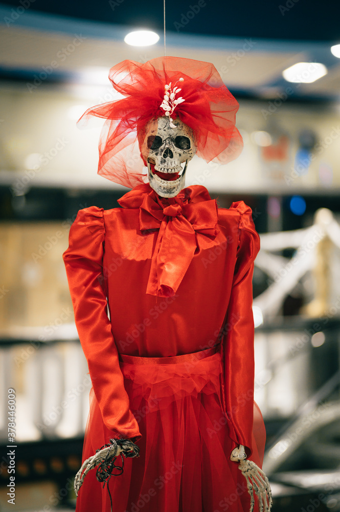 Skeleton of a woman in a red dress indoors, looking at the camera. Woman skeleton scenery for Halloween.