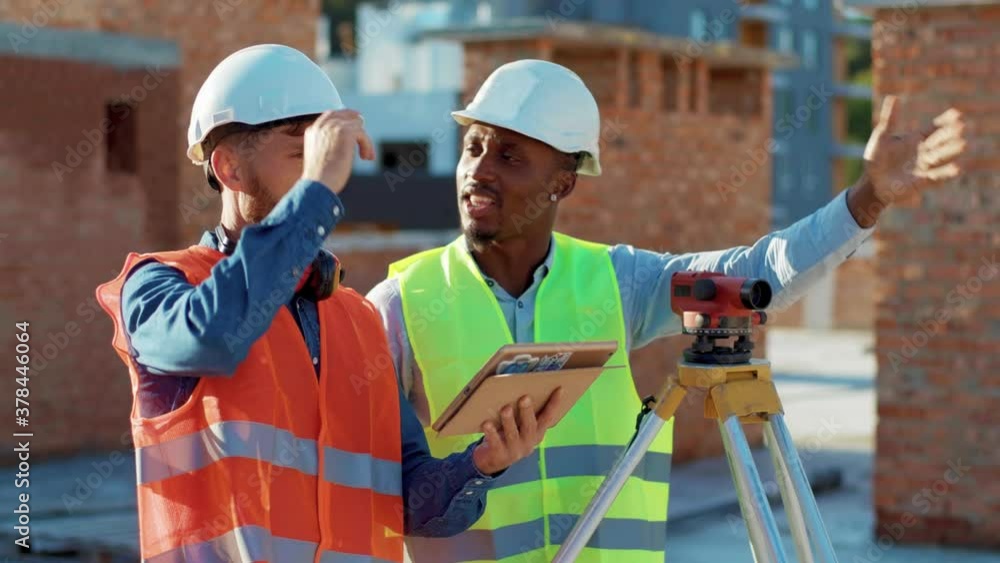Two men engineer surveyor discussing take measures with theodolite use tablet compute stand helmet hardhat geodesy building digital engineering african american infrastructure industry slow motion Two men engineer surveyor discussing take measures with theodolite use tablet compute stand helmet hardhat geodesy building digital engineering african american infrastructure industry slow motion
