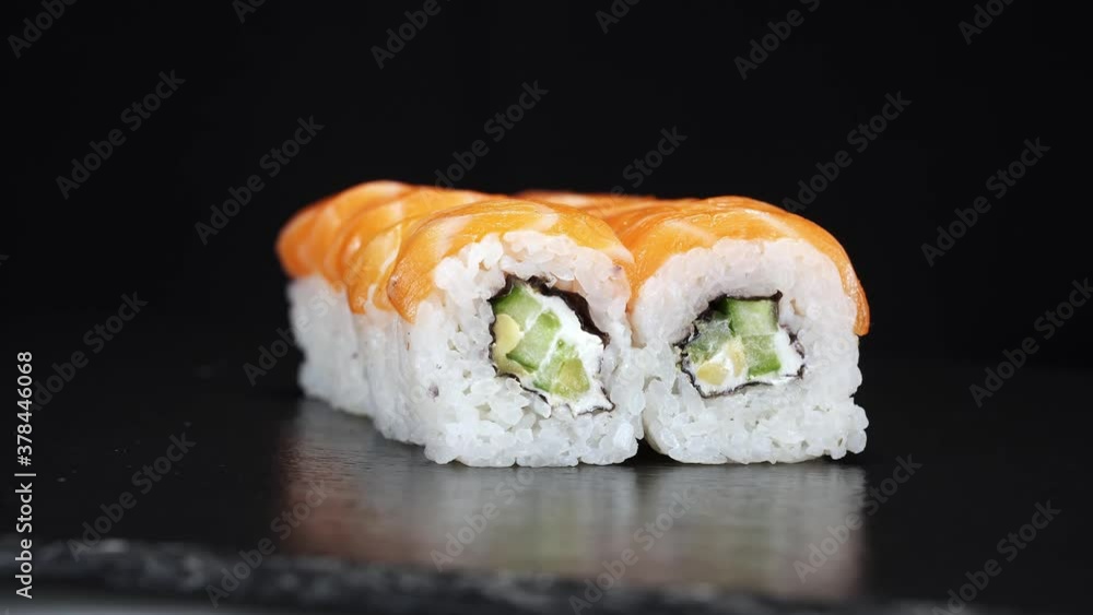 Sushi rolls rotate on black background. Close-up shoot. Philadelphia cheese, cucumber and salmon in Japanese food. Tasty asian food. Sushi rolls rotate on black background. Close-up shoot. Philadelphia cheese, cucumber and salmon in Japanese food. Tasty asian food.