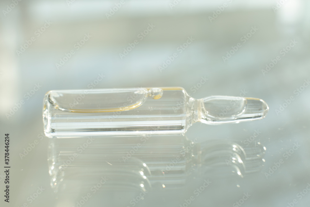 A glass vial with a solution lies on a glass table A glass vial with a solution lies on a glass table