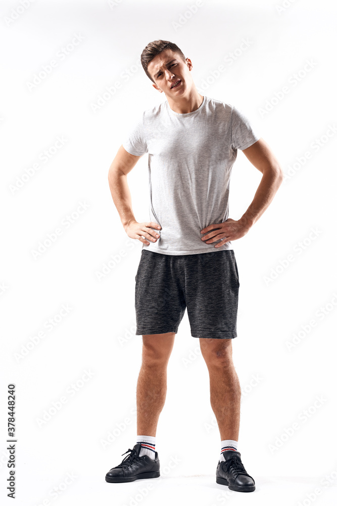A sports man in shorts and a full-length T-shirt does exercises on a light background A sports man in shorts and a full-length T-shirt does exercises on a light background