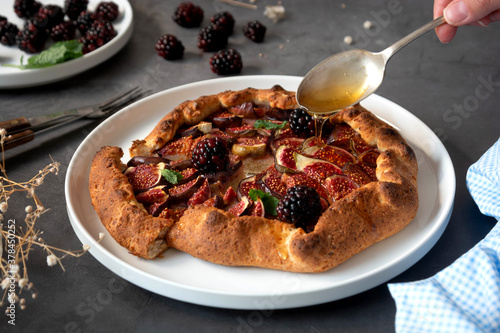 Figs galette. Hand pouring honey over traditional rustic fruit homemade pie  top view.